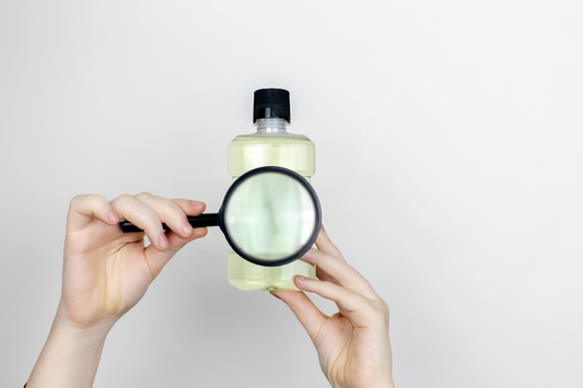 Person holding a bottle of skincare product with a magnifying glass, symbolizing scrutiny of harmful ingredients like parabens, sulfates, and synthetic fragrances.