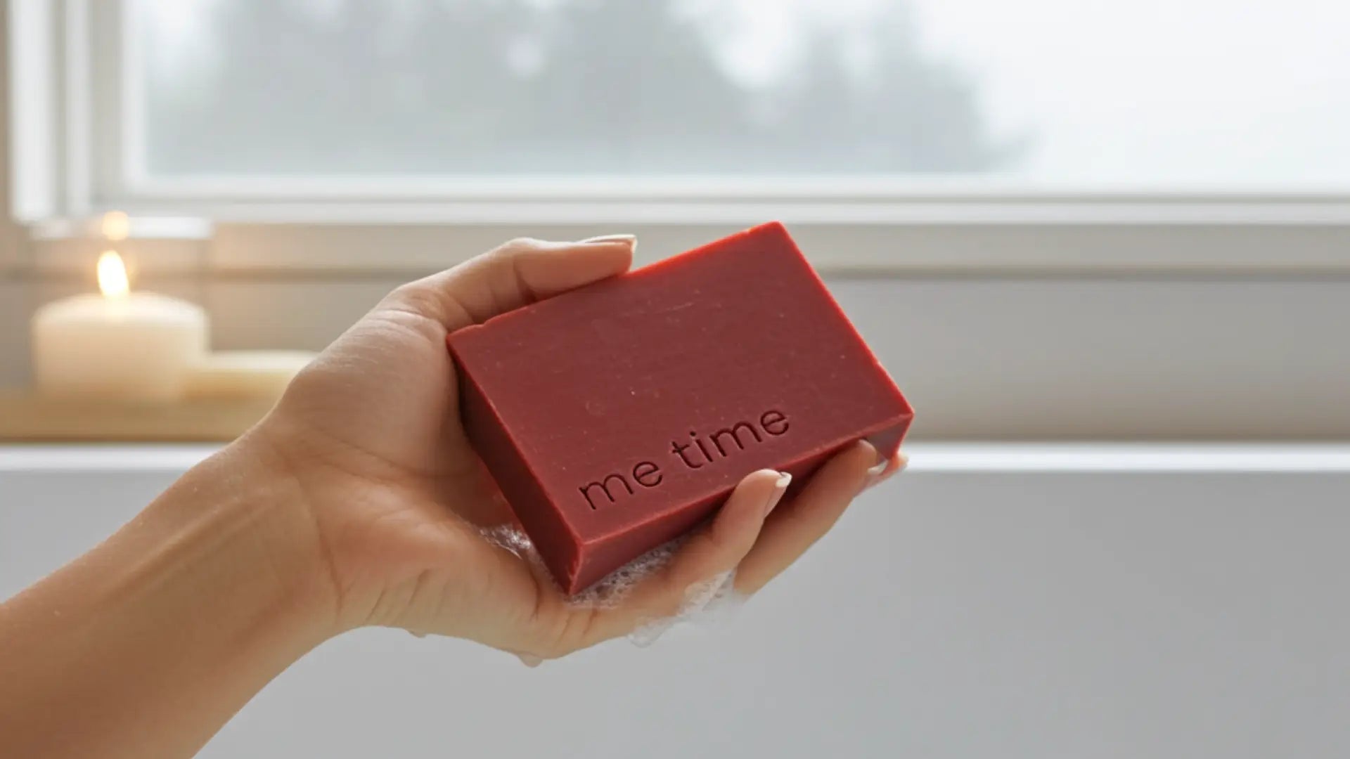 Hand holding a red bar of soap with 'me time' text, blurred window in the background